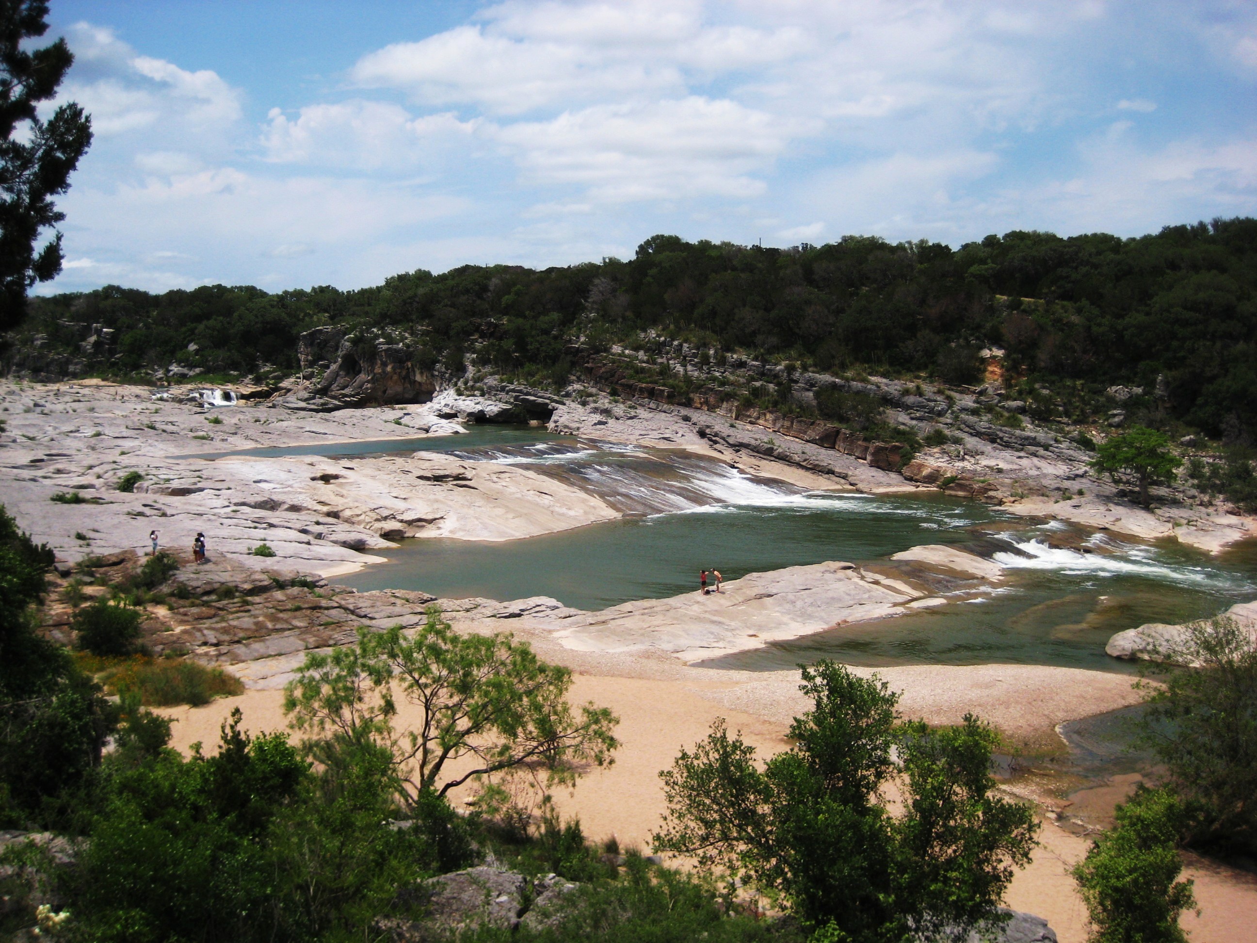 The stepped limestone ledges of Pedernales Falls State Park in the Texas Hill Country, where the Pedernales River drops over honey-colored rock shelves in a series of cascades surrounded by juniper and live oak